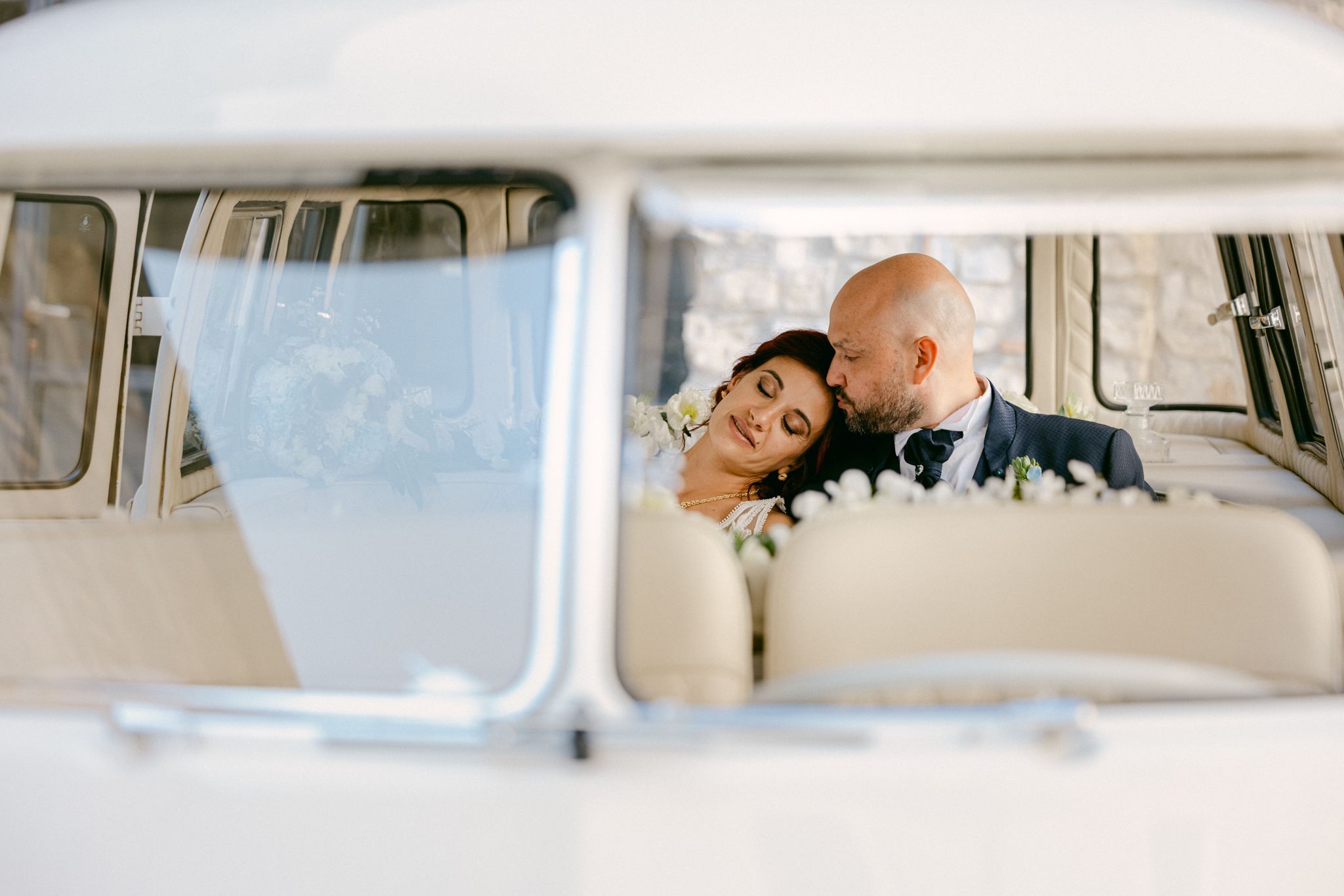 Bride and groom share a romantic moment inside a vintage white VW camper van on their wedding day.