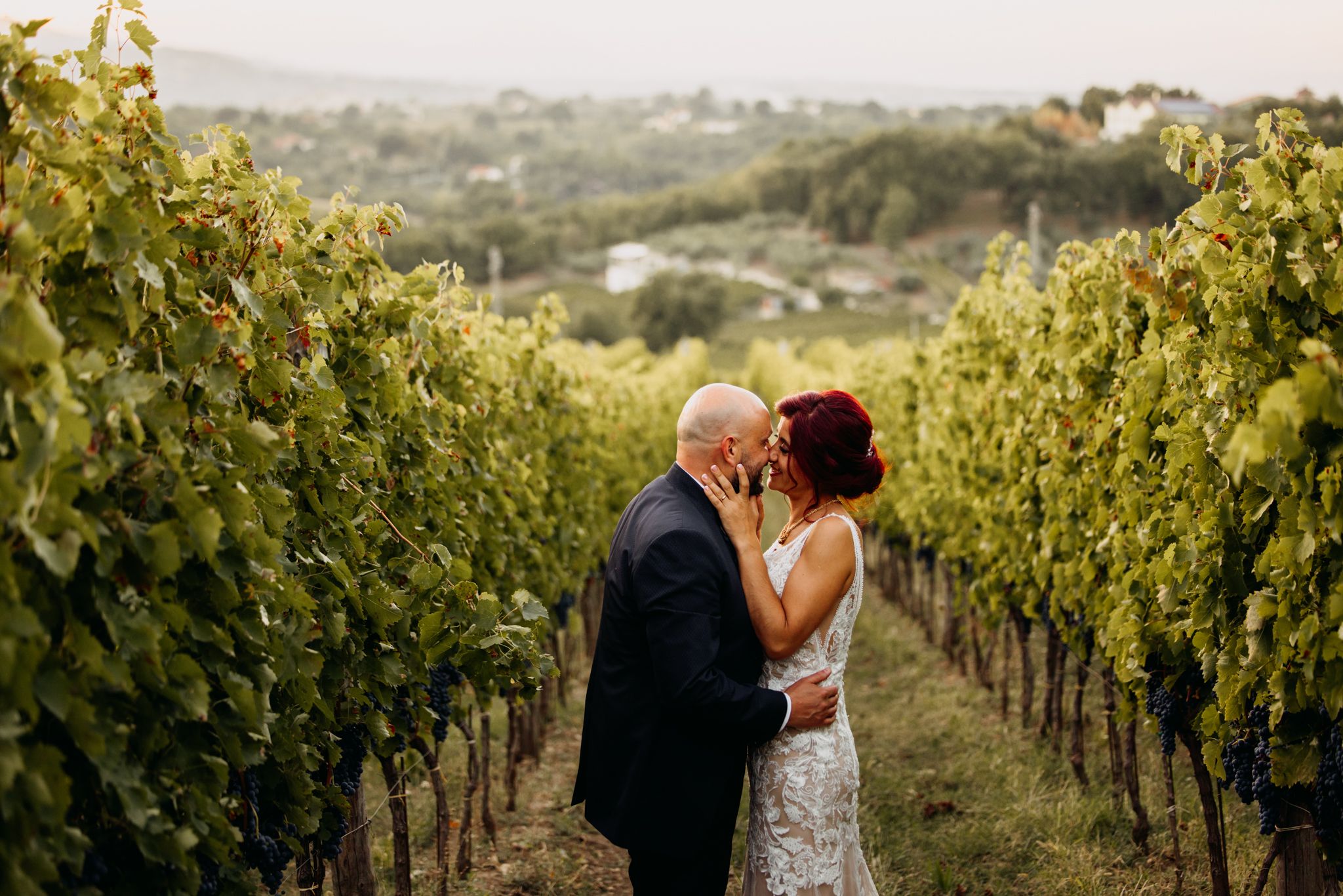 Couple shares a tender kiss among lush vineyard rows during their romantic outdoor wedding celebration.