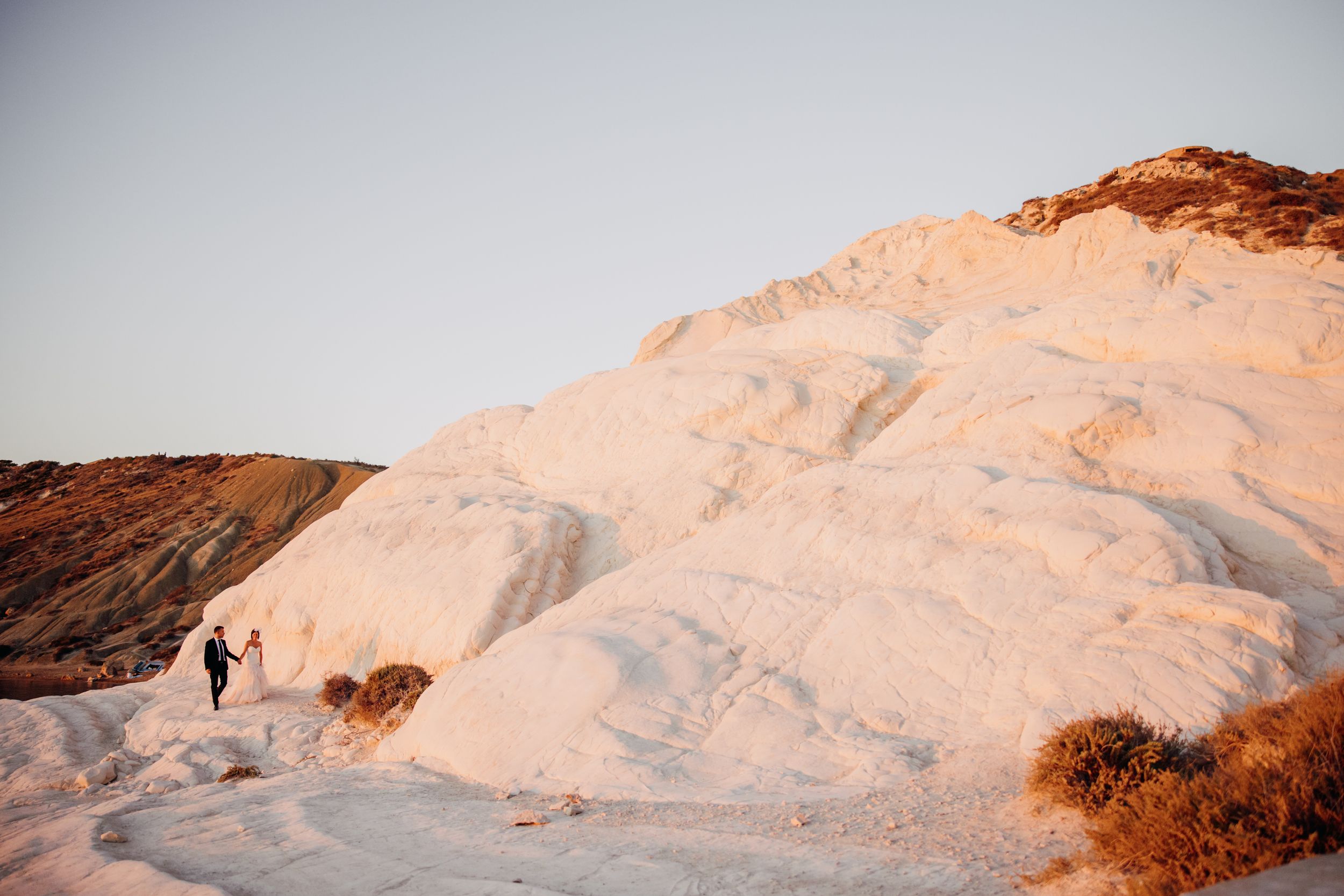 Wedding couple walking along white chalk cliffs at golden hour in a scenic landscape.