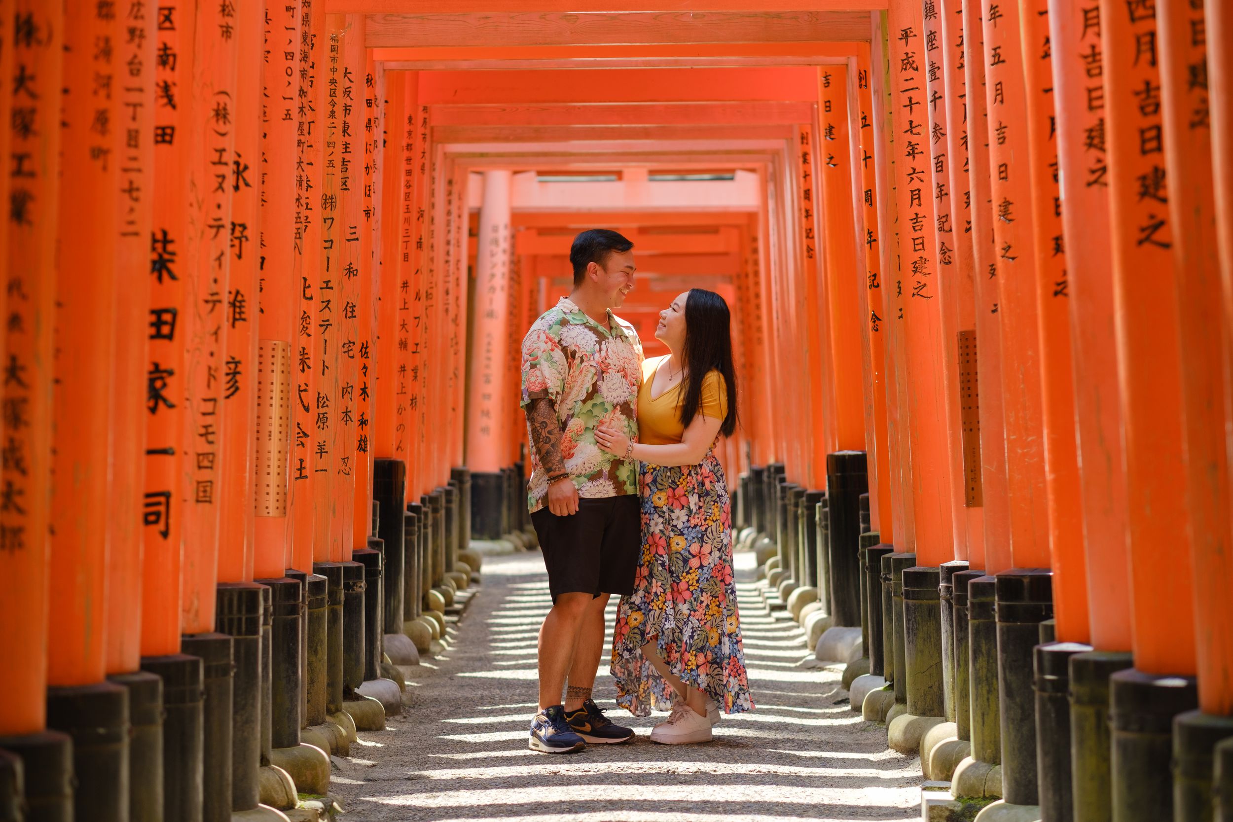 Couple embraces and gazes at each other on a stone path beneath the orange torii gates of Fushimi Inari shrine in Kyoto.