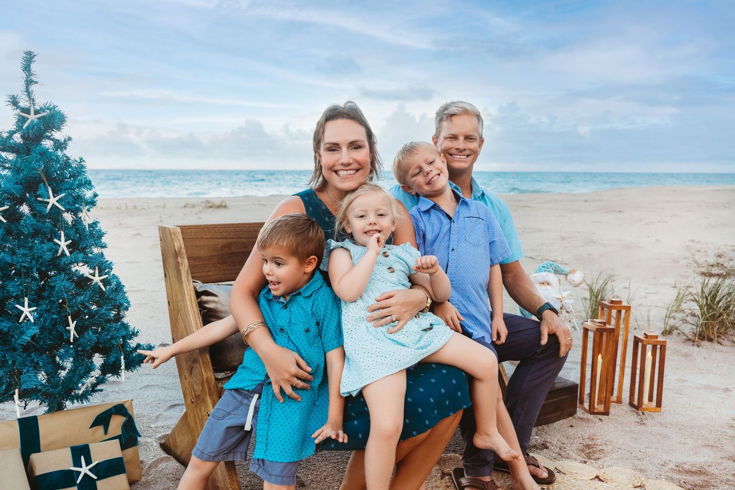Family on a beach beside a teal Christmas tree during a tropical Christmas mini session on Florida’s Treasure Coast.