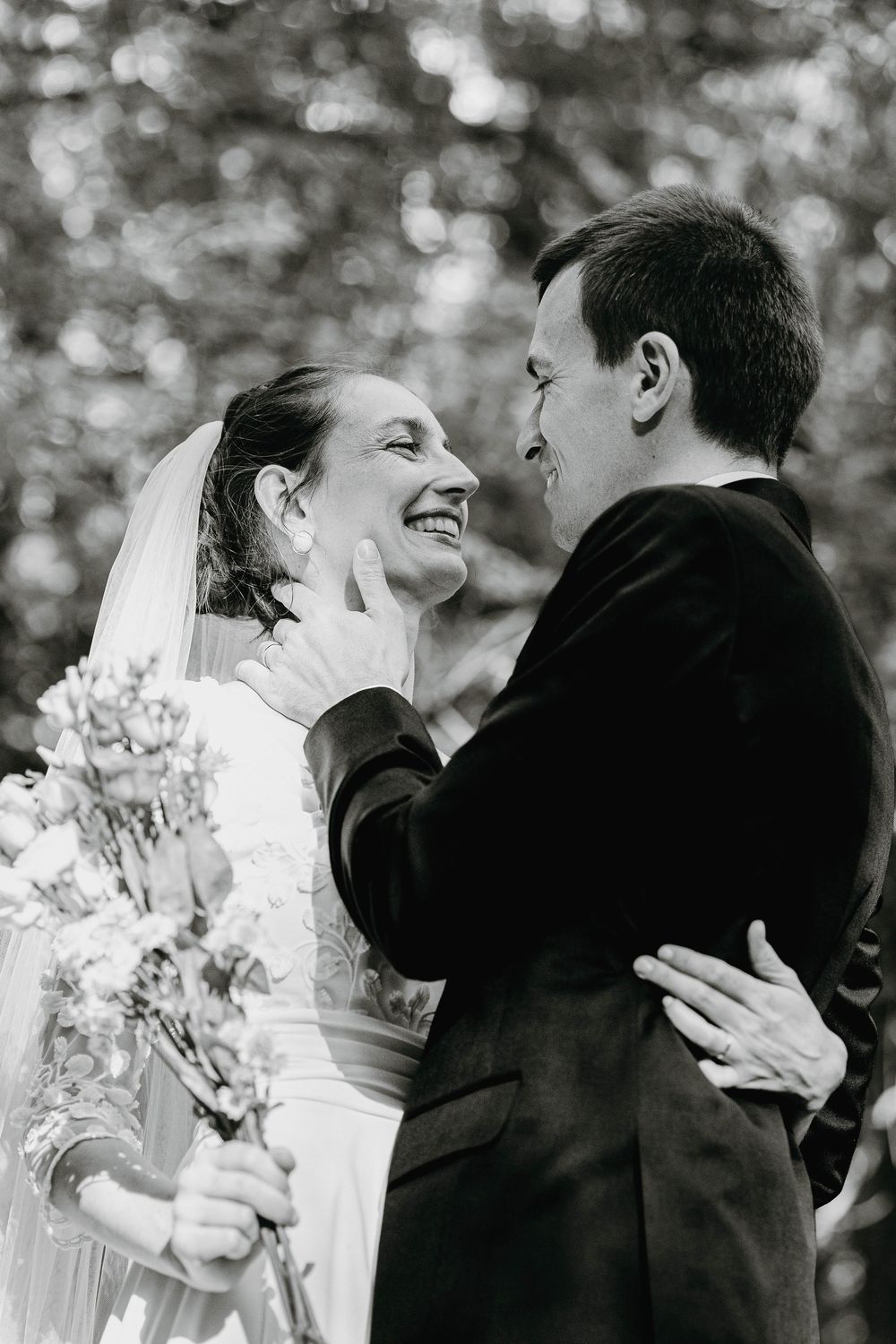 Black and white photo of groom touching brides face as she smiles joyfully.