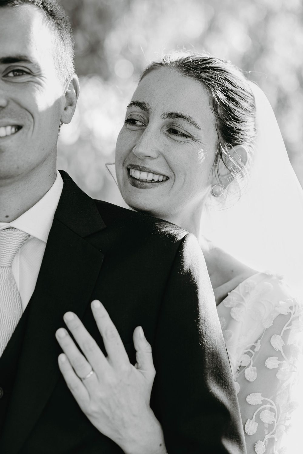 Black and white portrait of a smiling bride leaning against her groom in a suit and tie.