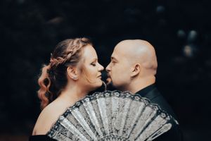 Egy szerelmes pár csókolóznak egy díszes ezüst legyező mögött egy meghitt esküvői portréfotózás során.