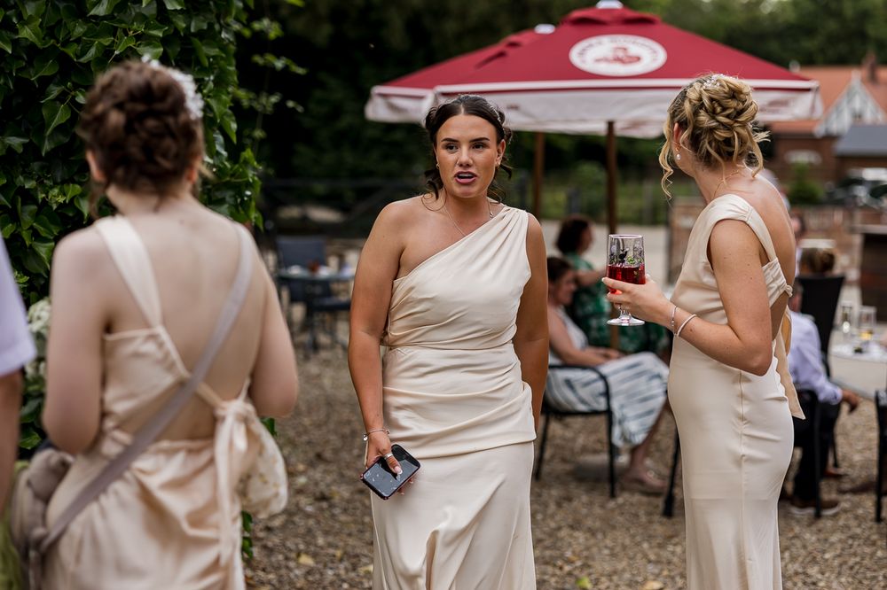 Three bridesmaids in elegant champagne satin dresses socializing outdoors at a wedding reception.
