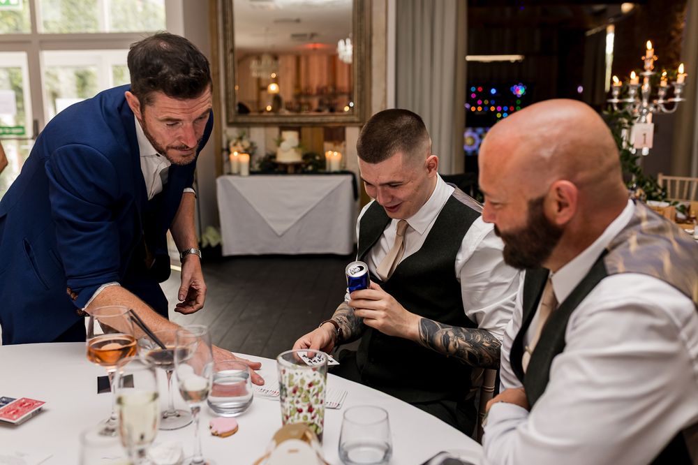 A magician performs a card trick for two guests at a wedding reception dinner table.