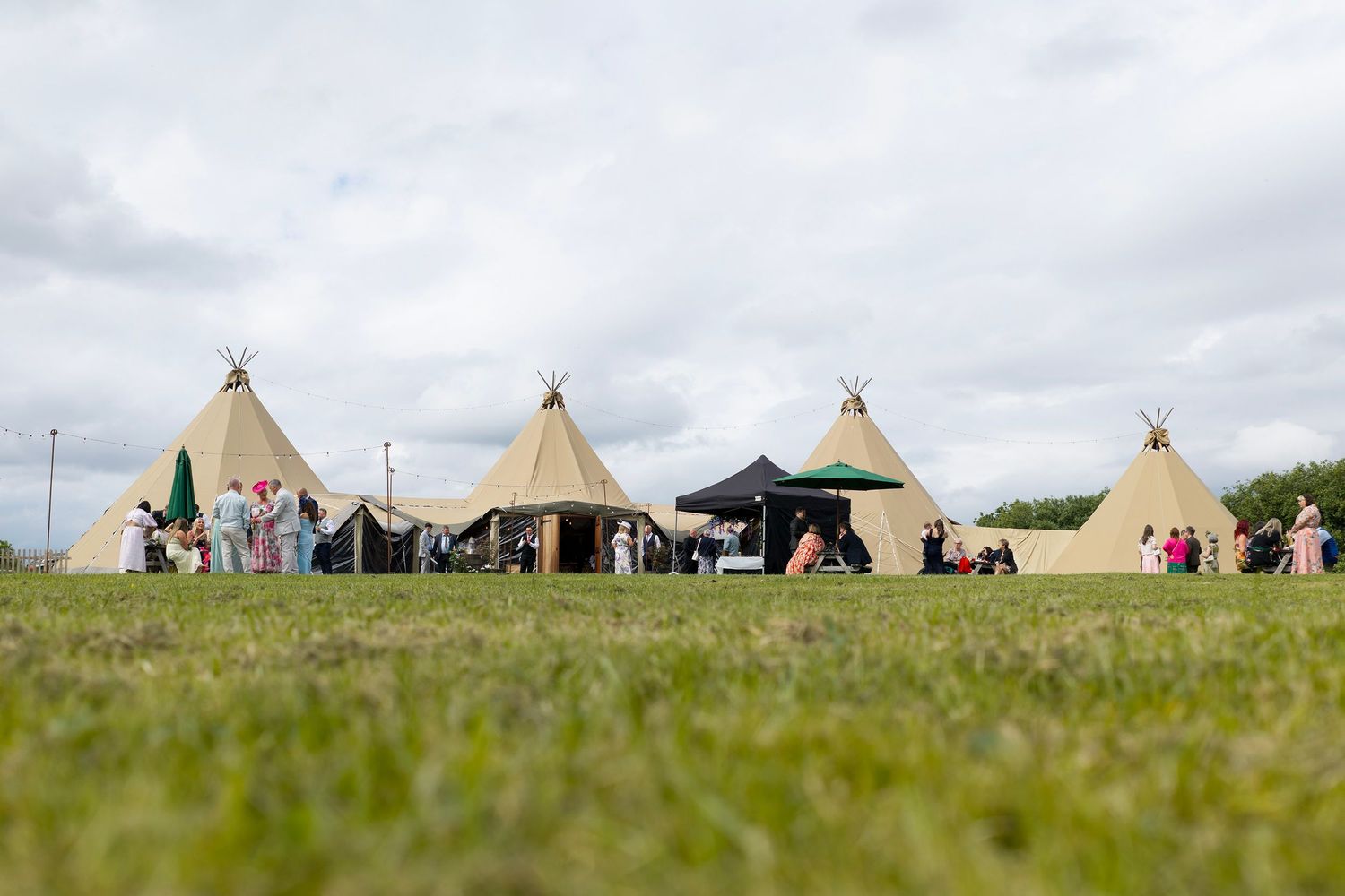 Low view across the lawn towards the giant tipis and wedding guests at The Den at Four Acre near Wigton.