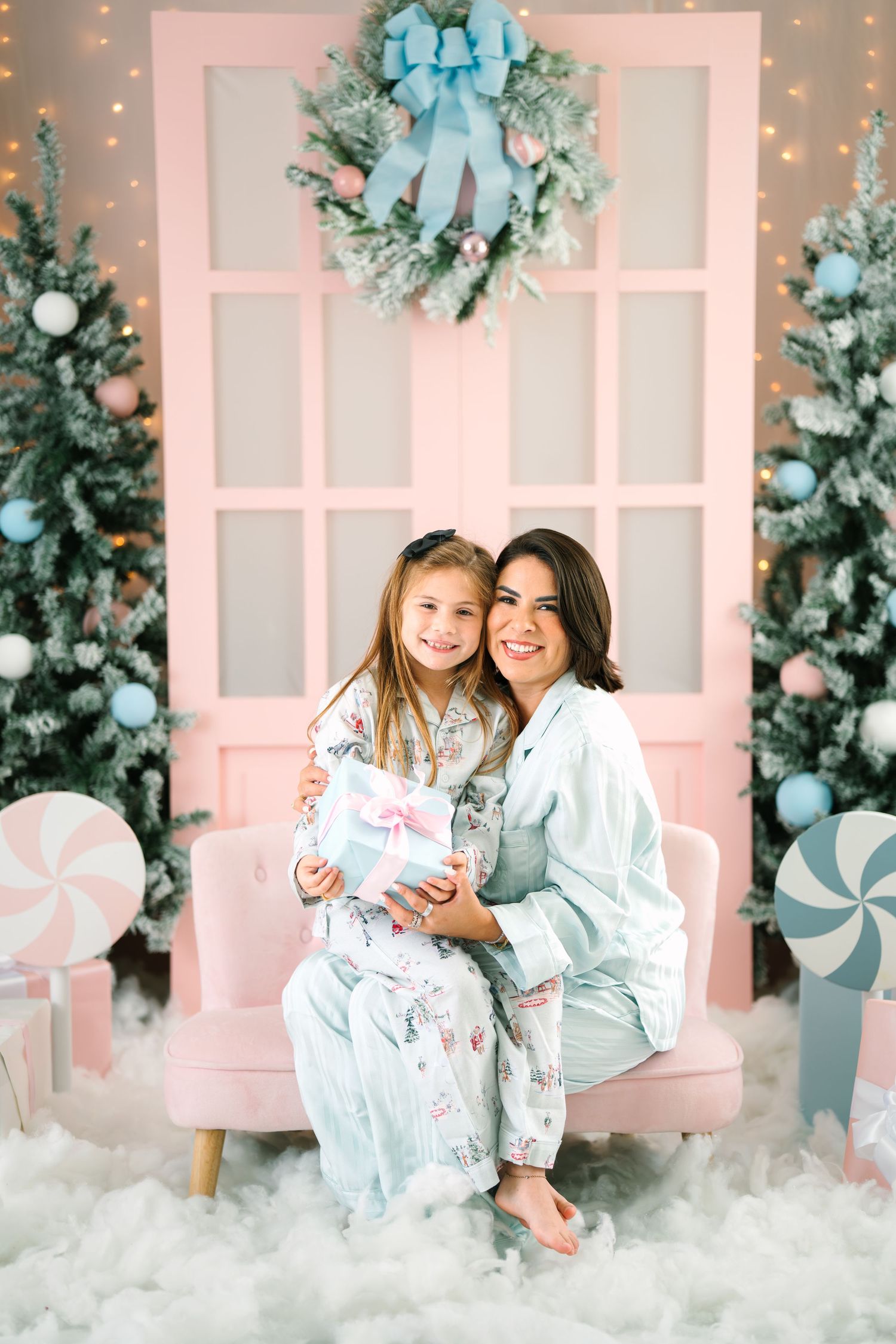 Mother and daughter in matching pajamas holding a Christmas gift in a festive pink holiday decorated room.