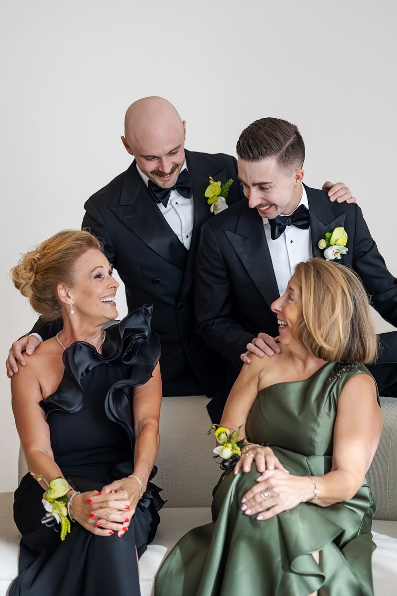 Two men in tuxedos and two women in formal gowns share a joyful moment together at a wedding celebration.