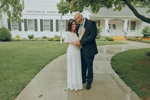 Smiling couple embracing on a curved walkway outside a Southold Town building, the bride in a white dress and the groom in a dark suit.