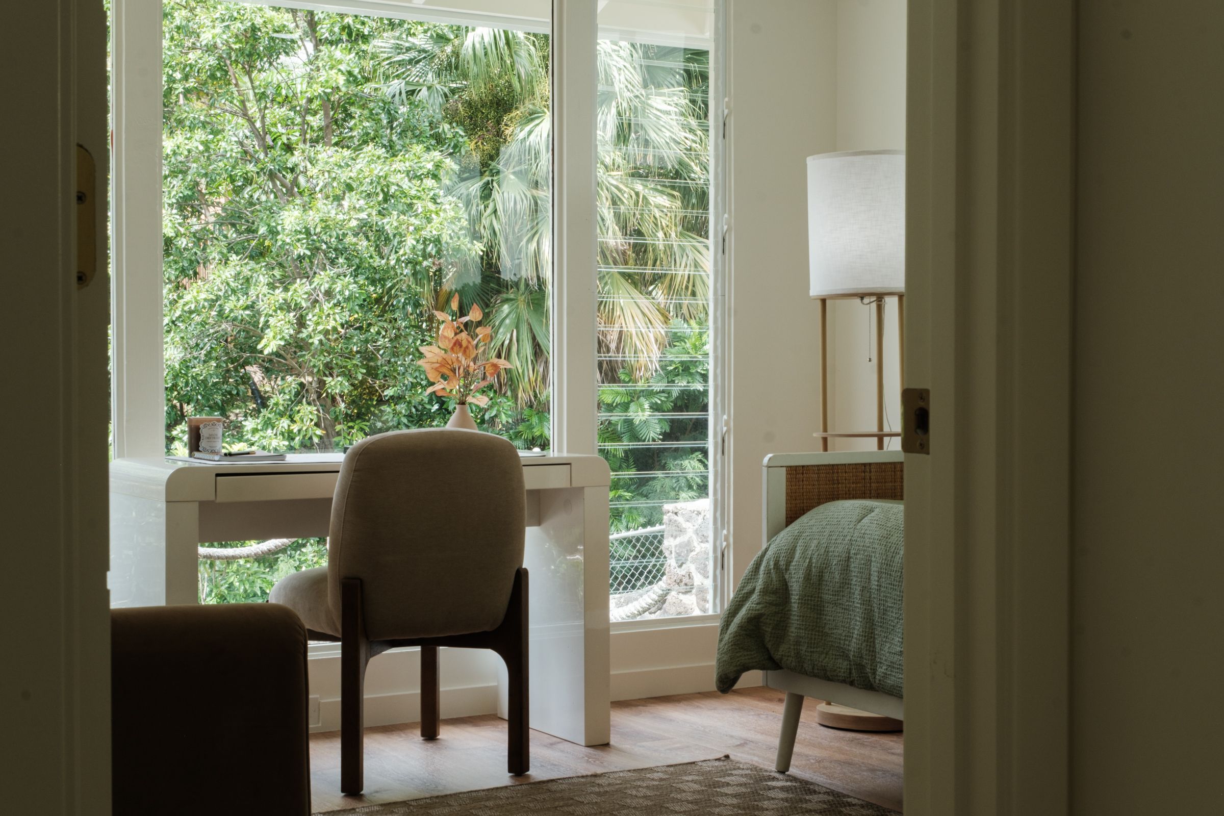 View through a doorway into a home office with a desk, upholstered chair, and garden-facing windows.