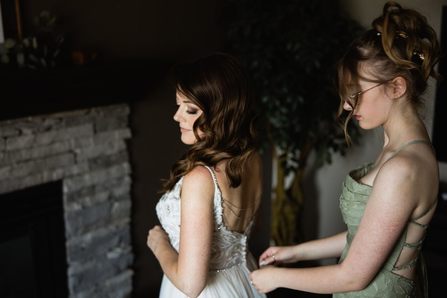Bridesmaid adjusting the bride's gown beside a stone fireplace