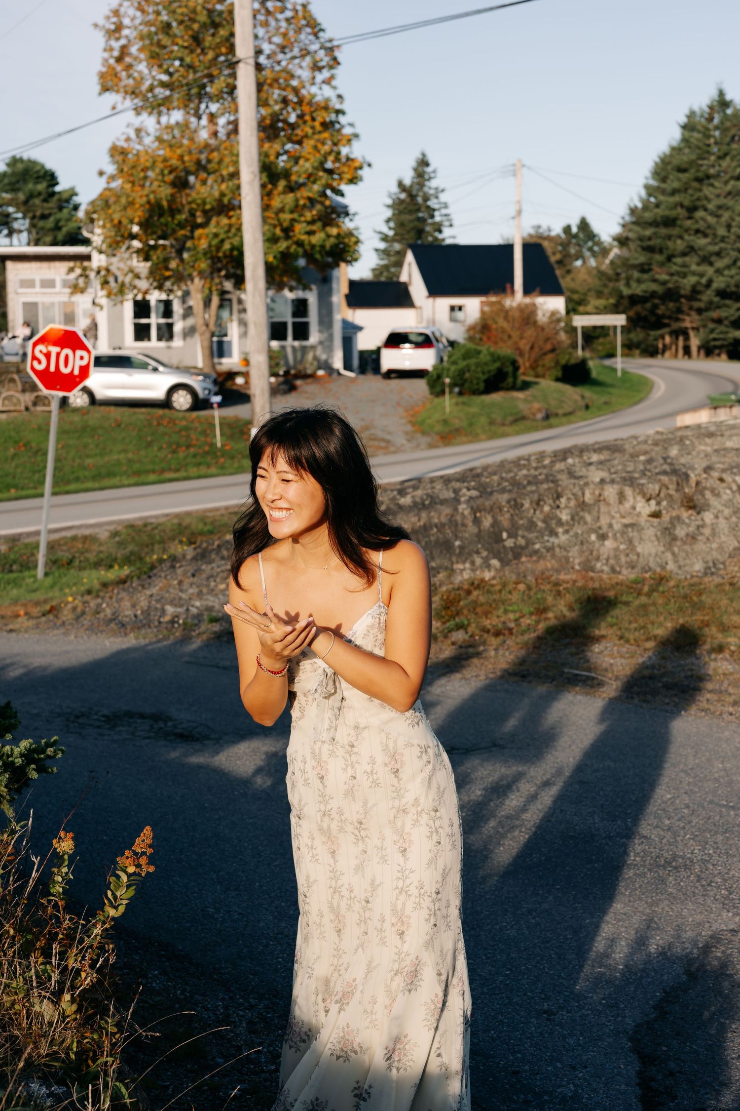 Smiling young woman in floral sundress standing near a stop sign on a sunny day with houses and trees in the background in Nova Scotia