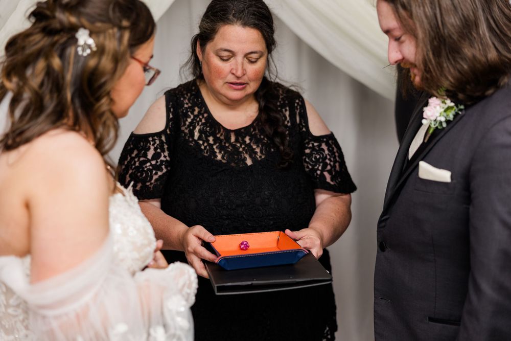 Wedding officiant holds ring box as bride and groom exchange rings during intimate indoor ceremony.