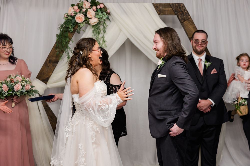Bride and groom share a joyful moment at the altar during their wedding ceremony with floral arch backdrop.