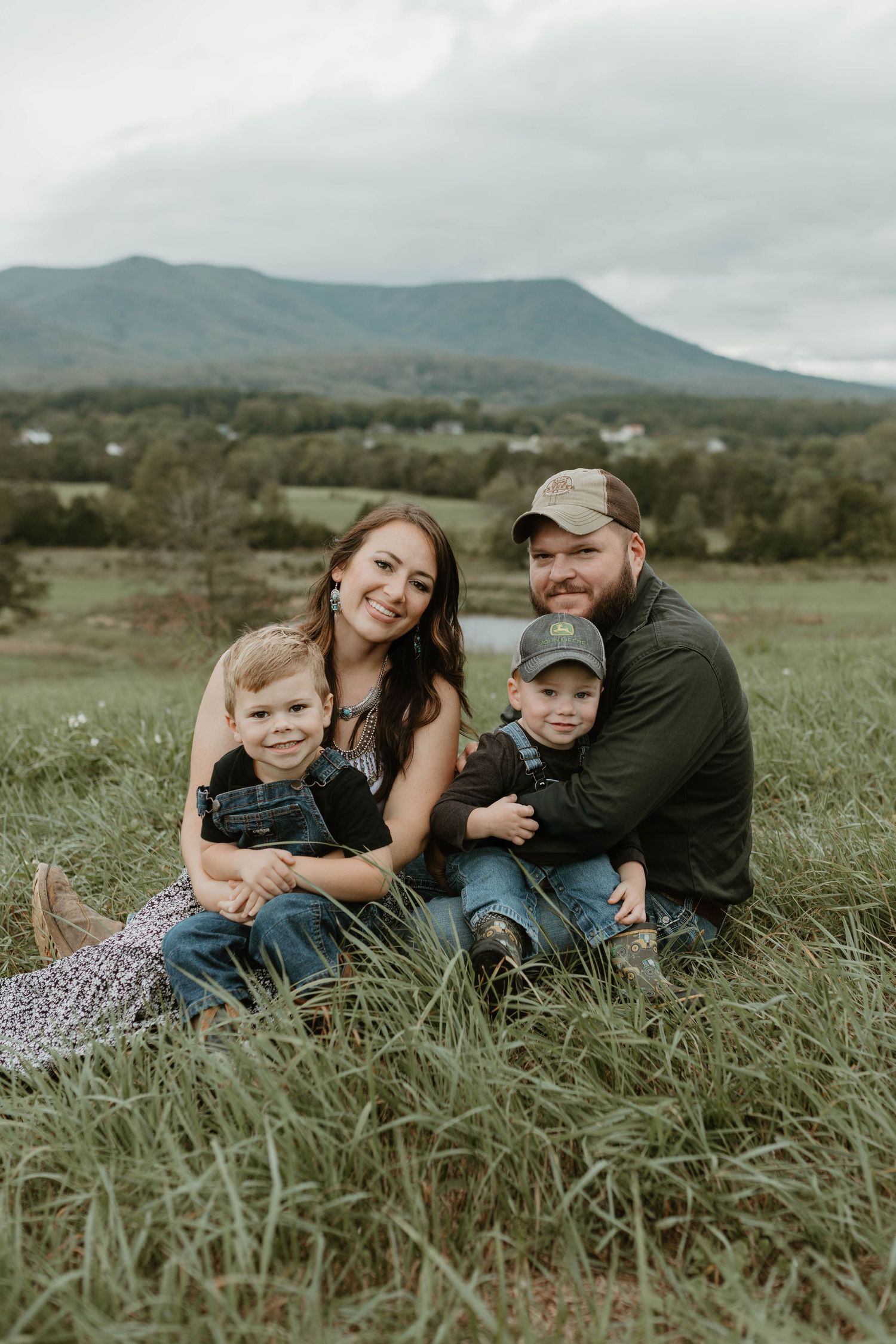 Family lying together in tall grass with mountain landscape in background.