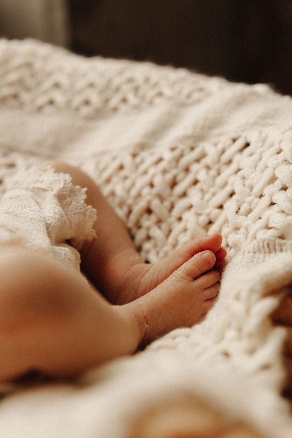 Close-up shot of tiny baby feet resting on a white knitted blanket with soft natural lighting.