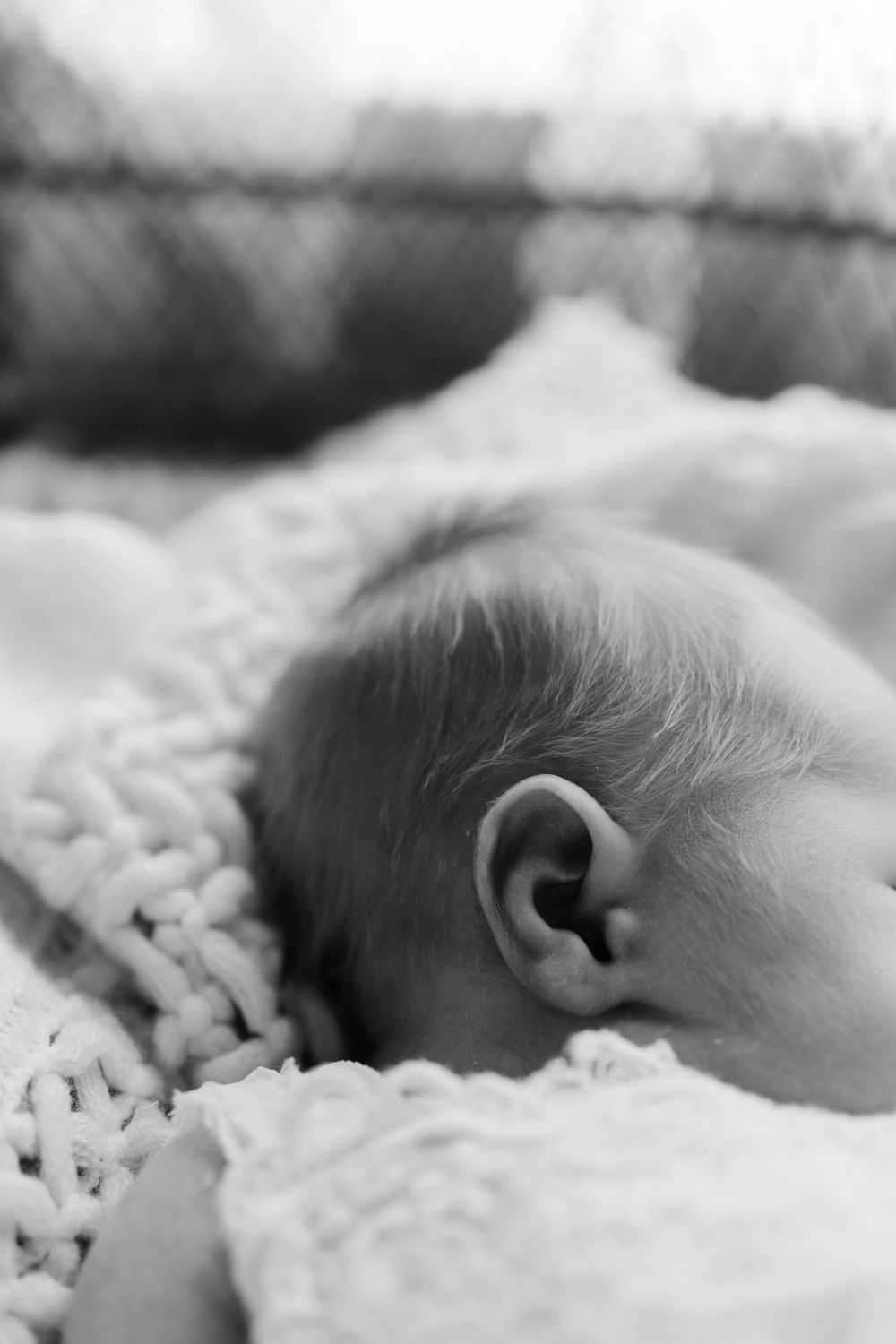 A sleeping newborn baby rests peacefully on soft textured white bedding in black and white.
