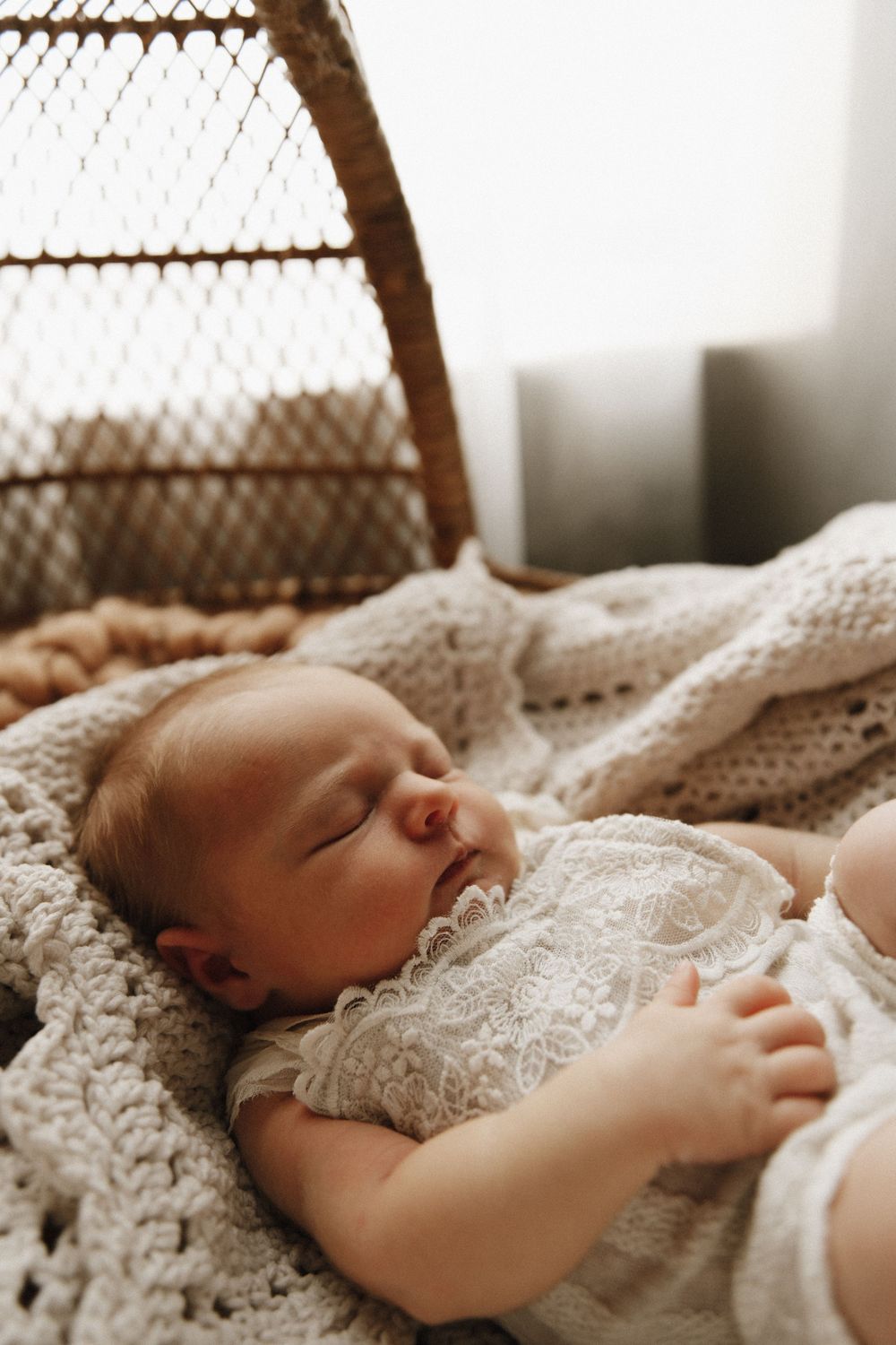 A sleeping baby rests peacefully in soft lace bedding while sunlight filters through a latticed window above.