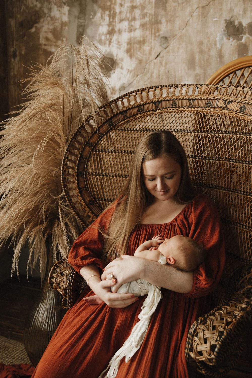 Rustic maternity photography series with pampas grass decor and peacock chair showing tender moments in warm rust tones.