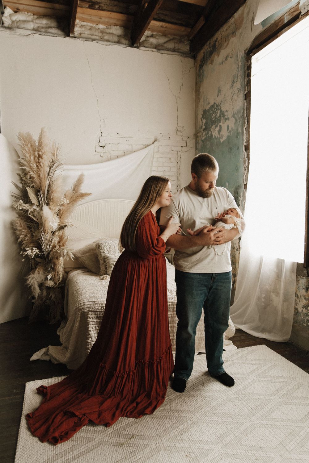 A maternity photo session in a rustic studio shows figures in burgundy dress and neutral clothing against white backdrops.