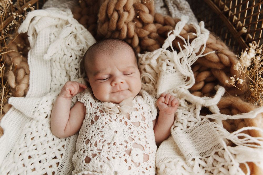 A baby sleeps peacefully on white crocheted lace blankets surrounded by vintage-style decor.