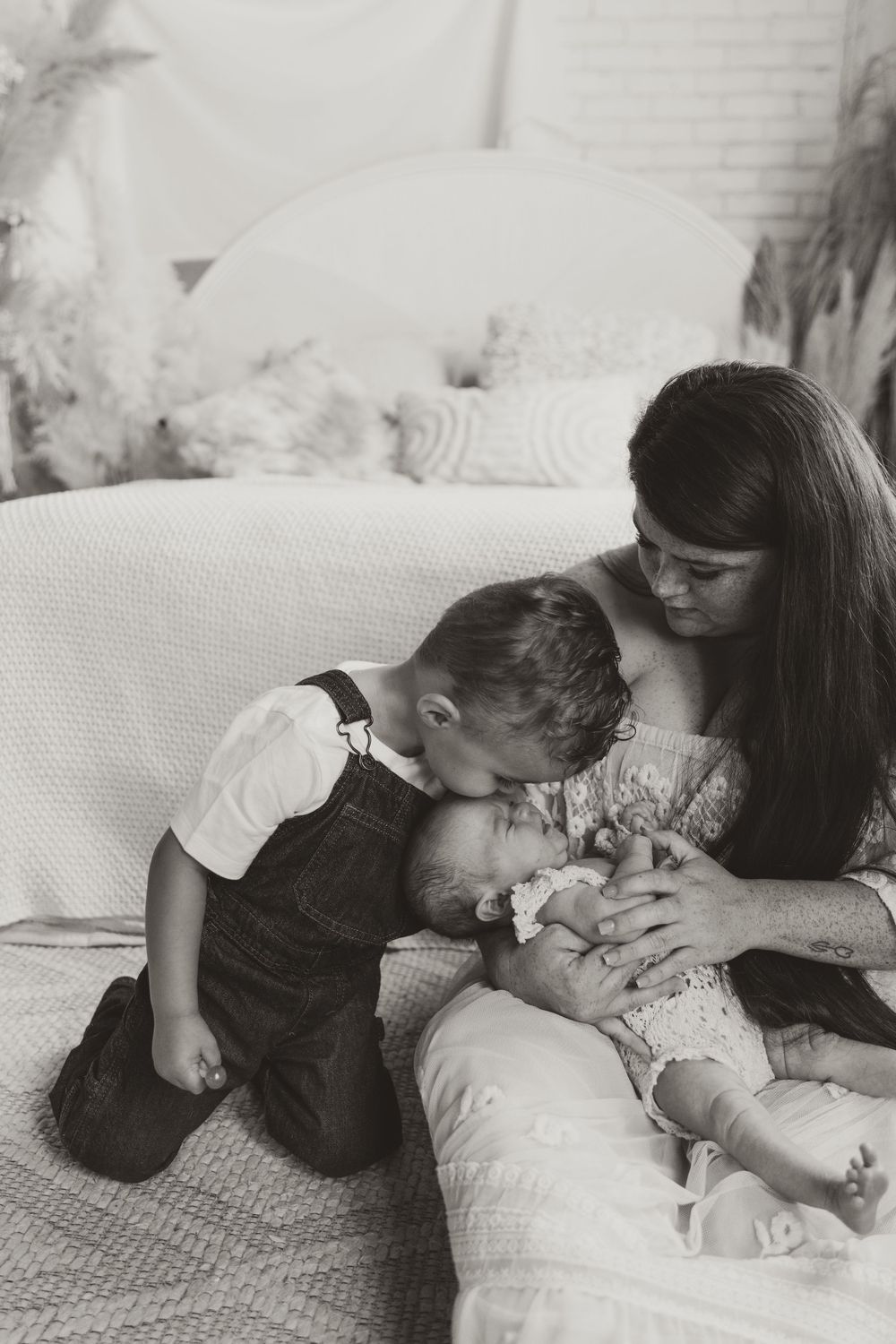 Black and white family photos showing tender moments between siblings with a newborn baby, arranged in a sequence.