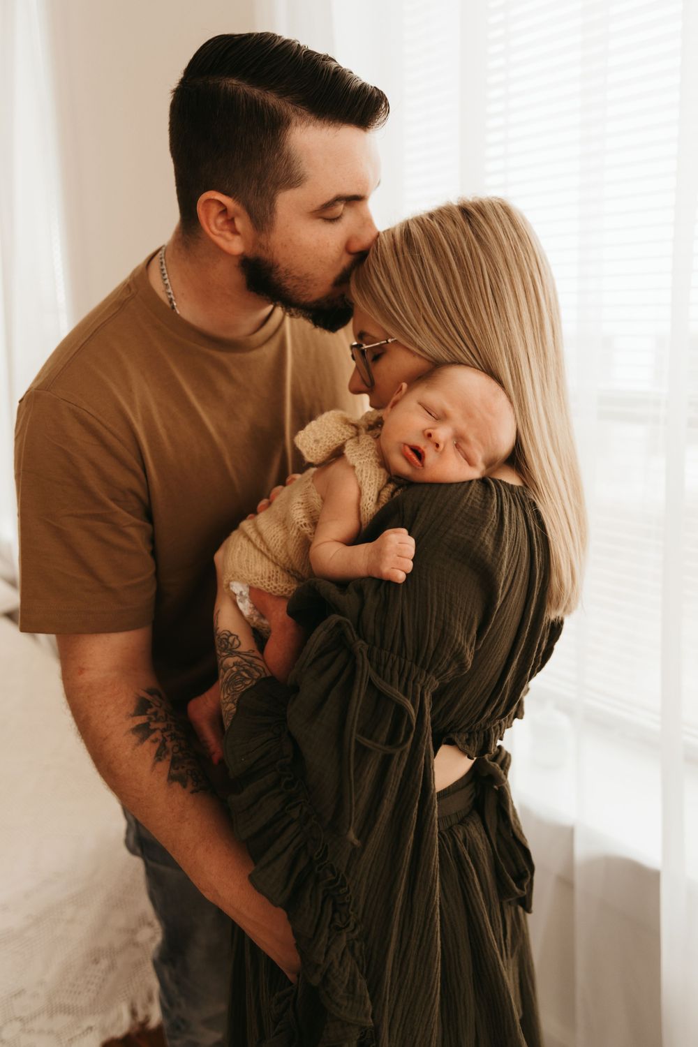 Family sharing tender moment with newborn baby in white room with natural light.