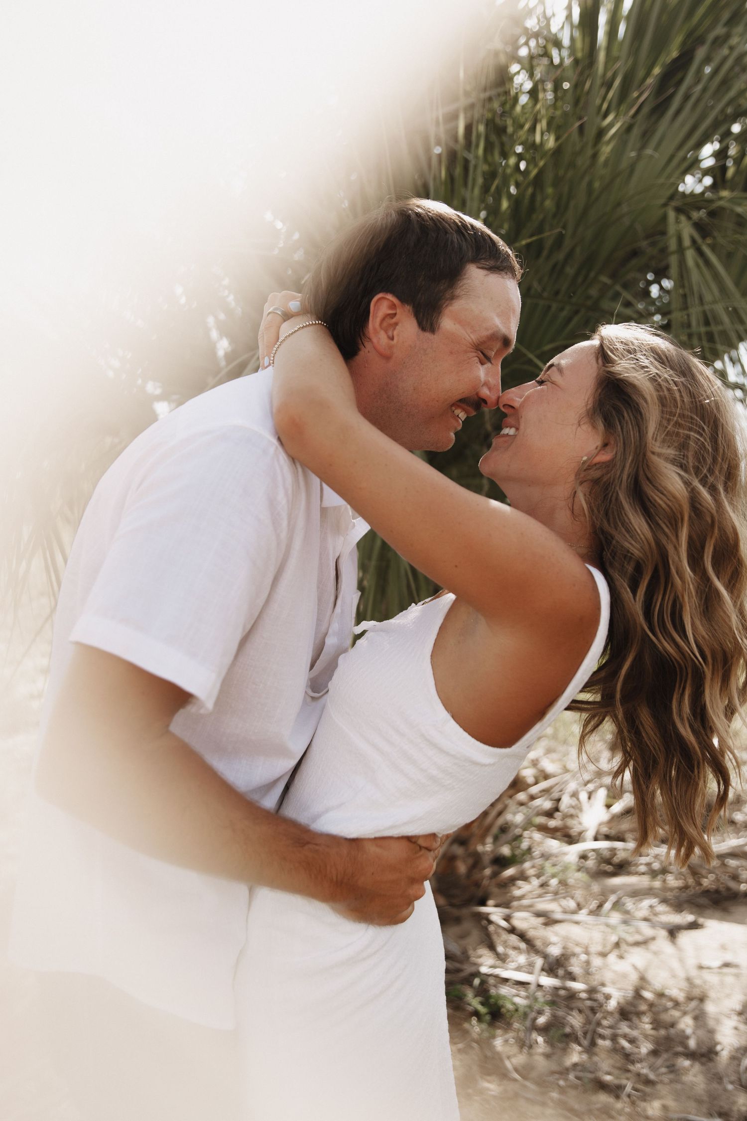 Romantic beach photo sequence of couple embracing and kissing in white outfits.