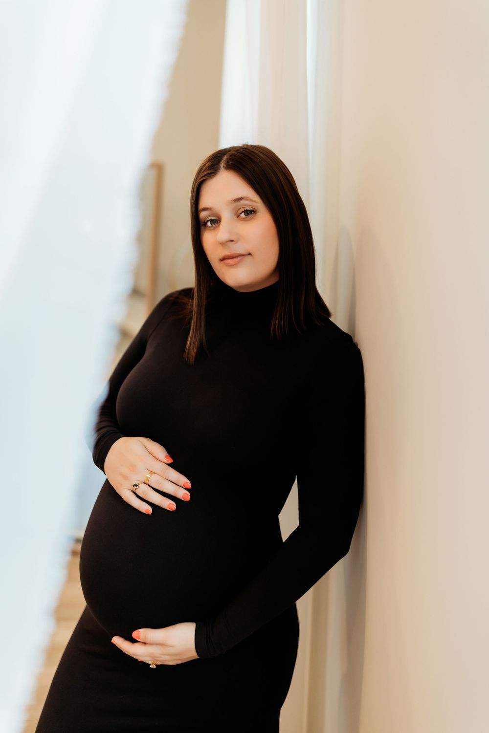 A series of maternity photos showing a pregnant woman in black clothing against a white wall.