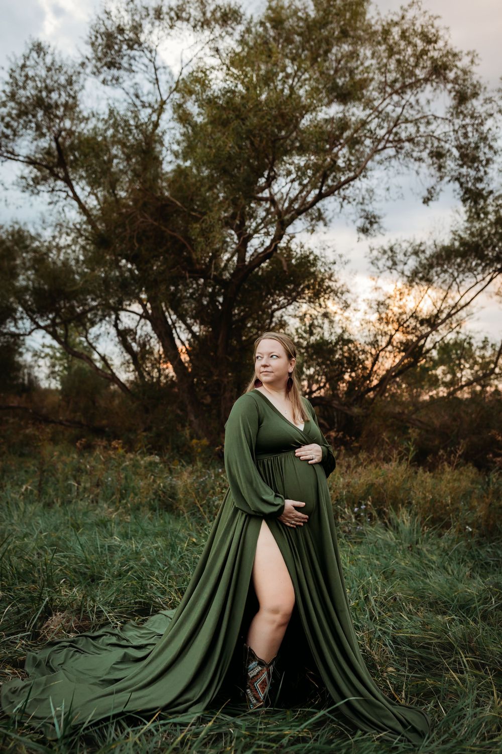 A flowing green dress billows dramatically across tall grass at sunset in an artistic outdoor portrait session.