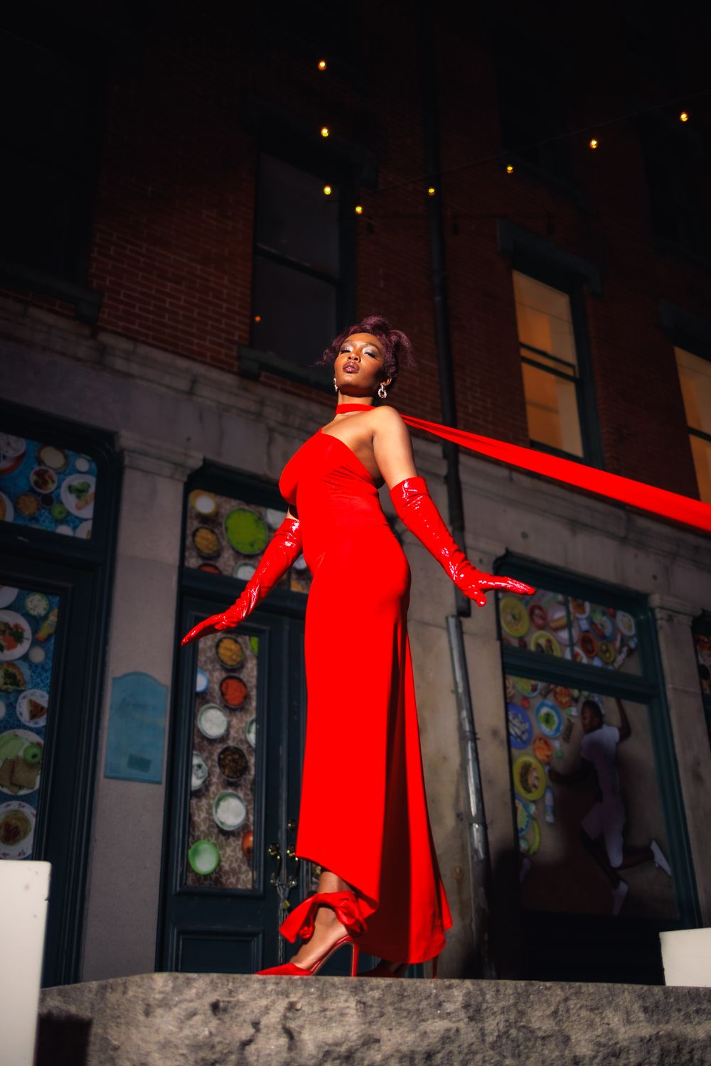 Dynamic fashion shoot featuring flowing red dress against urban brick wall backdrop.