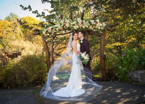 Autumn wedding portrait with flowing veil and golden foliage in background.