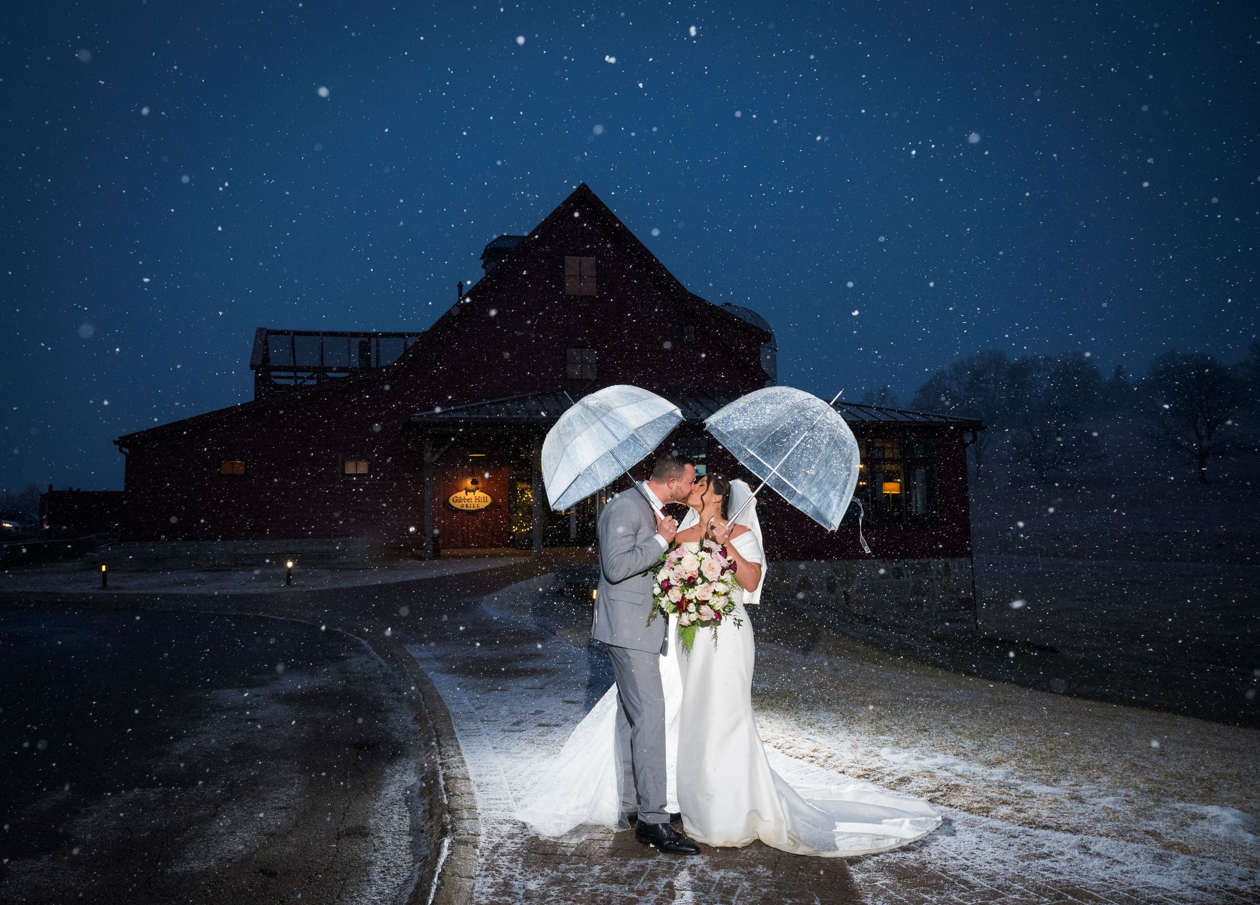 Romantic winter wedding photo with snowfall outside a rustic barn venue.