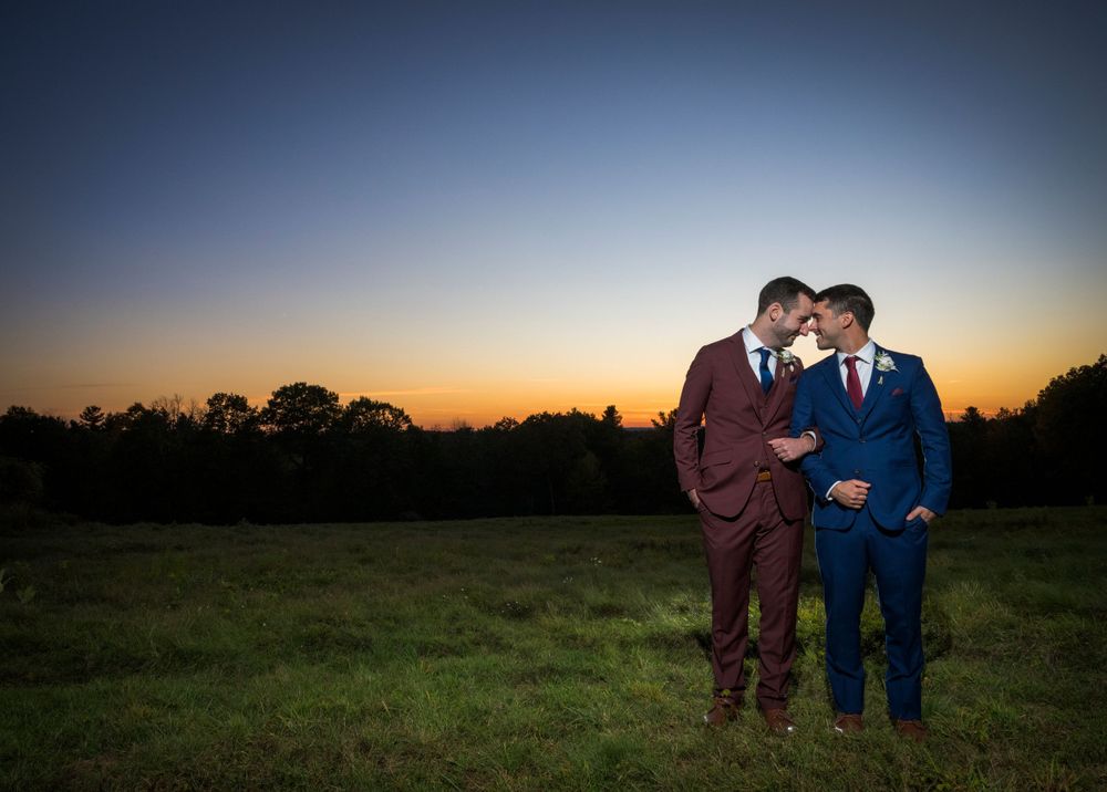 Romantic sunset wedding photo in an open field with dramatic orange and blue sky.