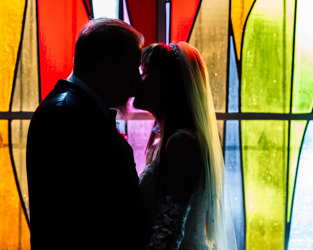 Wedding Couple kiss in front of stained glass window
