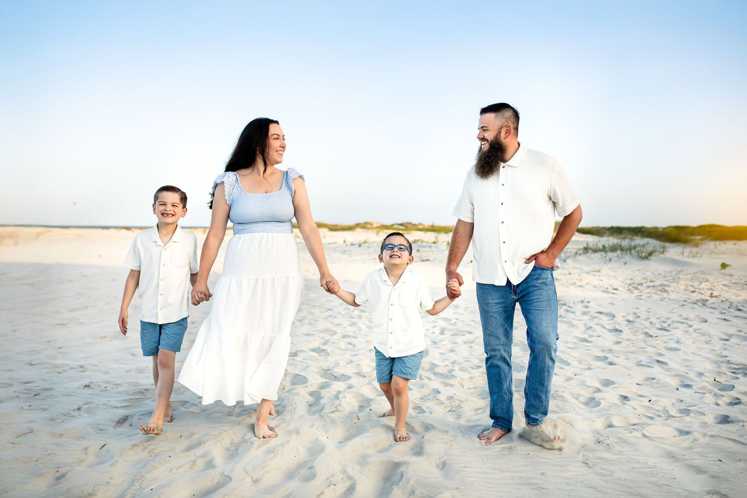 Family walking together hand in hand along a sunny beach shoreline at sunset.