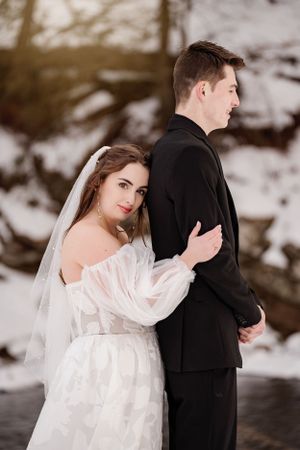 Bride and groom share intimate moment in winter wedding portrait against snowy backdrop.