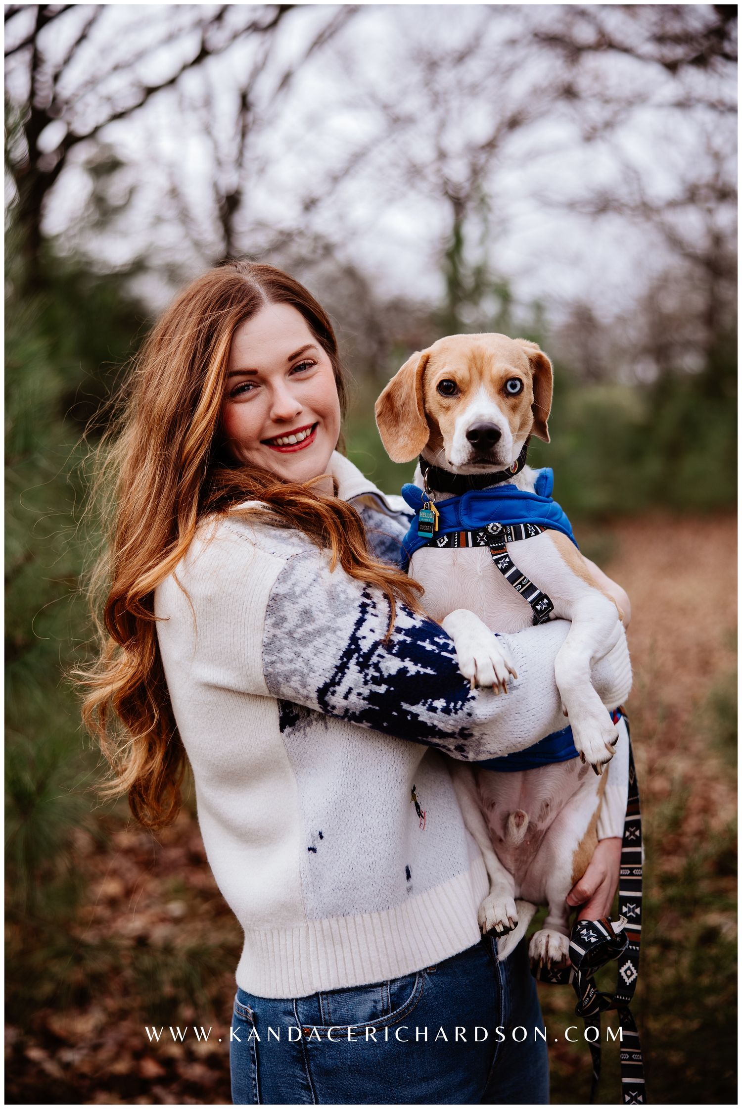 A white and brown beagle puppy wearing a blue bandana is held lovingly in a winter outdoor setting.