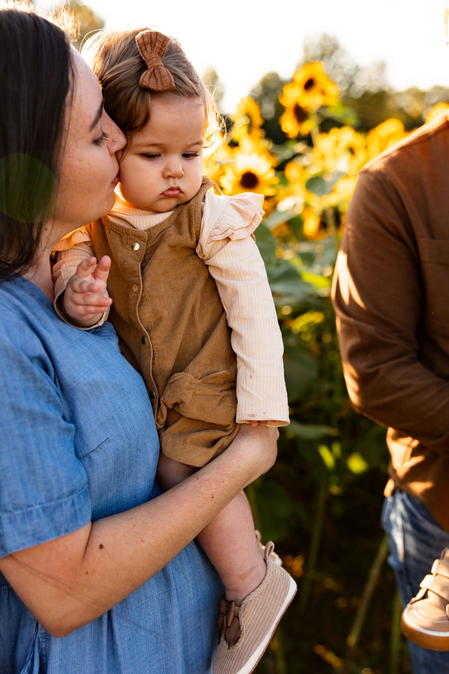 A tender family moment captured in a sunflower field during golden hour with warm sunlight illuminating the scene.