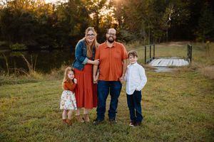 A group of people stand together in a grassy field during golden hour sunset for a fall family photo session.