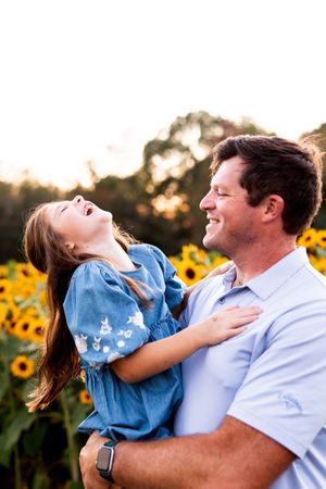 A series of joyful candid moments between a parent and child playing together in a sunflower field at sunset.