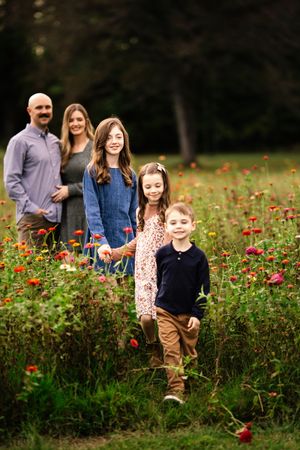 Family poses together in a vibrant wildflower field filled with red blooms on an autumn day.