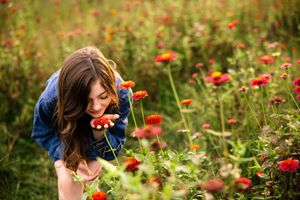 A person leans down to smell vibrant red and orange wildflowers growing in a lush green meadow.