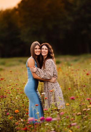 Two people share joyful moments together in a vibrant field of red wildflowers during golden hour.