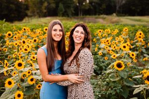 Two people stand together smiling in front of a vibrant field of blooming sunflowers during golden hour.