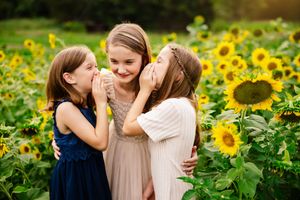 Three young sisters share secrets and giggles together in a vibrant summer sunflower field. Arkansas Photographer