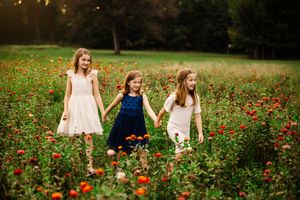 Three sisters walk hand in hand through a vibrant wildflower meadow at sunset. Arkansas Photographer