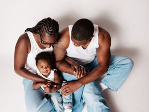 Loving family in matching white tank tops and jeans share intimate moment on white background.