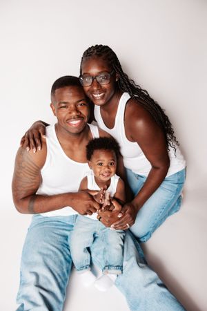 Beautiful family wearing coordinating white tops and jeans poses against white backdrop.